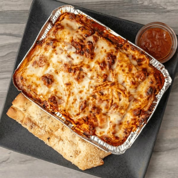 Baked spaghetti in a foil pan with garlic bread and a side of marinara sauce.
