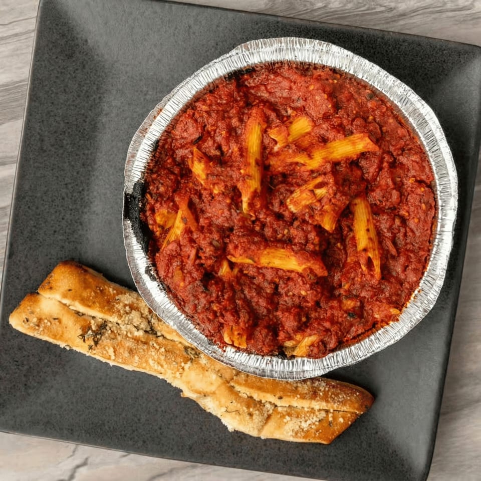 Baked penne pasta in red sauce in a foil tin, with a side of garlic bread.